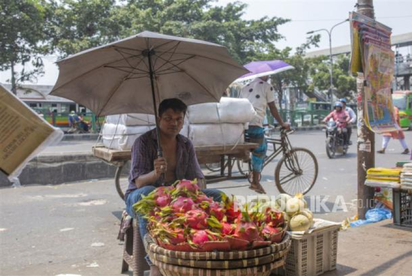  Pedagang memegang payung saat dia menjual buah-buahan saat<a href=