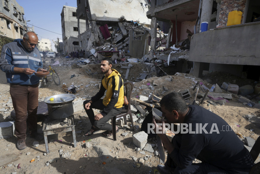 Warga Palestina memasak di depan reruntuhan gedung yang luluh lantak. 