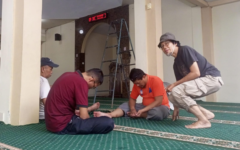 Jamaah membersihkan karpet masjid.