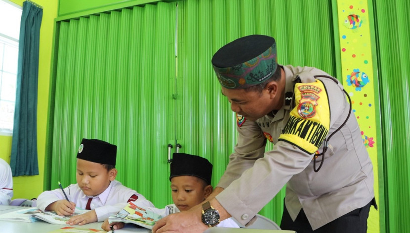 Aipda Minanto, personel Bhabinkamtibmas Polsek Blambangan sedang membimbing anak SD, Selasa (19/3/2024). (Foto: Dok. Polda Lampung)