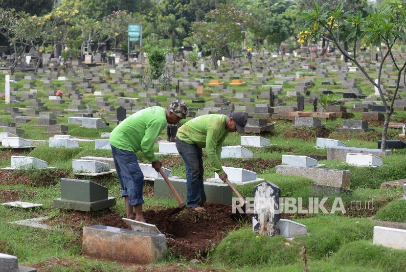 Dua orang pengurus makam sedang merapikan komplek pemakaman umum di Jakarta.