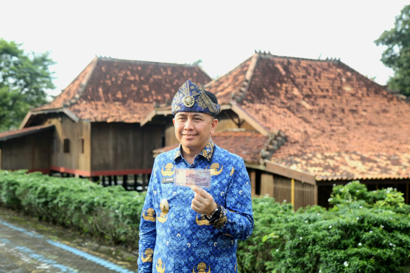 Agus Fatoni di Museum Negeri Balaputra Dewa dengan latar belakang rumah limas dan uang Rp10.000 di tangan. (FOTO: Humas Pemprov Sumsel)