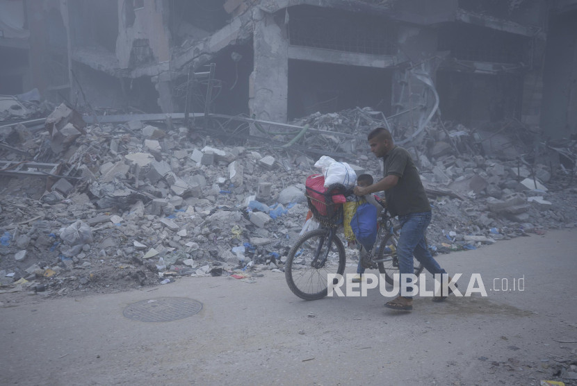 Warga Palestina berjalan di tengah puing-puing bangunan. 