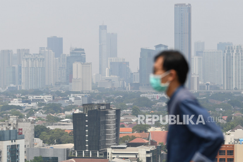 Warga mengenakan masker berlatar gedung bertingkat berselimut polusi. Paparan polusi udara dalam jangka panjang dapat meningkatkan risiko penyakit jantung, termasuk serangan jantung dan strok. Gambar: Republika