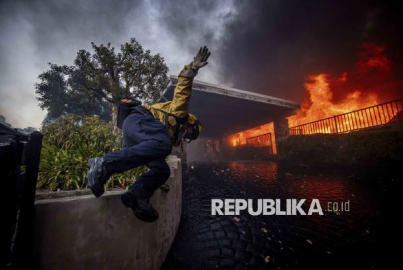 Petugas pemadam kebakaran melompati pagar saat berusaha memadamkan kebakaran besar yang melanda kawasan Pacific Palisades, Los Angeles, Kalifornia, Selasa (7/1/2025). Foto: AP Photo/Ethan Swope