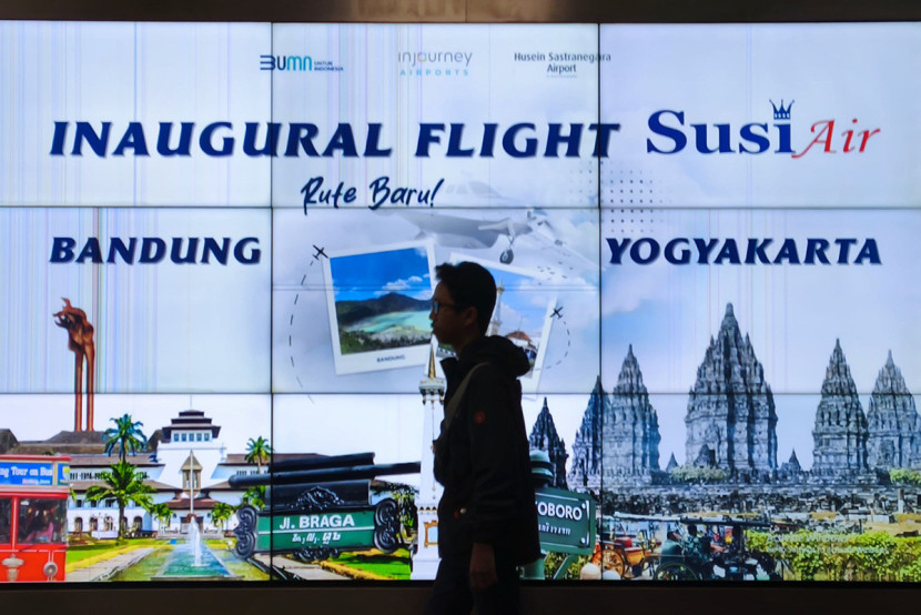 Seorang jurnalis melintasi videotron reklame penerbangan  Susi Air rute Bandung-Yogyakarta di Bandara Husein Sastranegara, Bandung, Rabu (2/7/2025).KANGJEPRET/YOGIARDHI (Data teknis: Olympus Pen F, Art Mode, Lumix 14-140/3.5-4.5)GUb