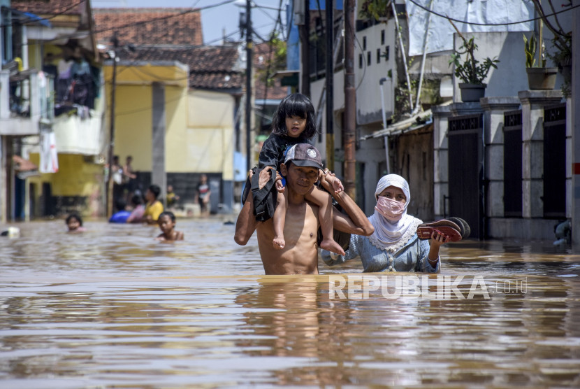Ilustrasi cuaca ekstrem, warga menggendong anaknya menerjang banjir.