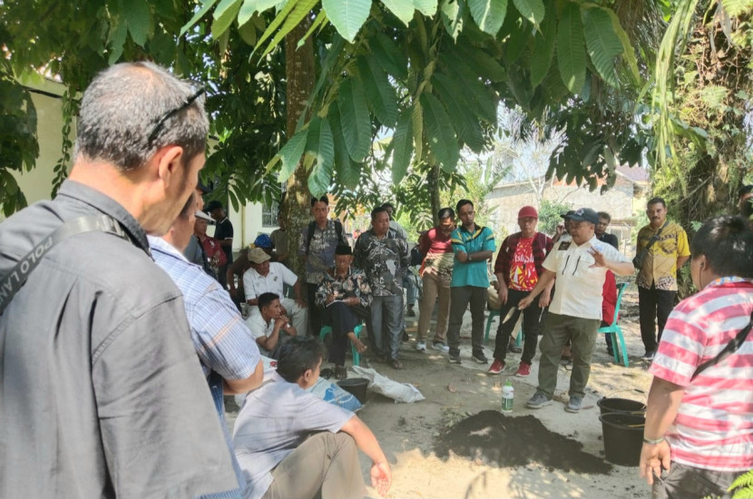 Praktisi biochar Arif Firmansyah yang juga Direktur PT Perfekta Lintas Semesta sedang mempraktekkan penggunaan biochar yang telah dicampur dengan kompos dan pupuk hayati ke pohon sawit di Desa Trimulya Jaya, Kecamatan Ukui, Kabupaten Pelalawan, Riau, Kamis (24/7/2025).