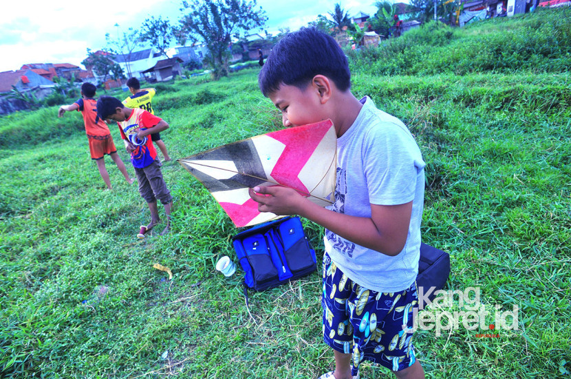 Seorang anak memasangkan tali timba sebelum menerbangkan layang-layang di tanah lapang Lingkung Cai Kel Kujangsari, Bandung Kidul, Kamis (31/7/2025). Kangjepret/Yogi Ardhi (Data Teknis Nikon D3, Nikkor AF 20mm f/2.8 D).