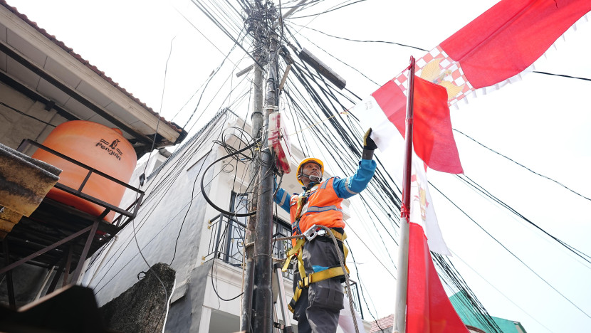 Petugas PLN sedang merapikan bendera dekorasi 17-an yang menempel dengan jaringan listrik. Pemasangan seperti ini berisiko tinggi dan tidak aman. (Foto: Dok PLN)