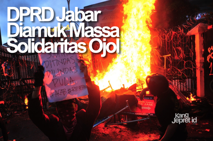 Pengunjuk rasa membentangkan poster protes dengan latar api besar di pintu gerbang Gedung DPRD Jawa Barat, Jumat (29/8/2025). Mereka memprotes kematian Affan Kurniawan penemudi ojol yang dilindas Kendaraan Taktis (Rantis) Brimob di Jakarta. (KANGJEPRET.ID/YOGI ARDHI) (Nikon D3, Nikkor 20mm/2.8 D).