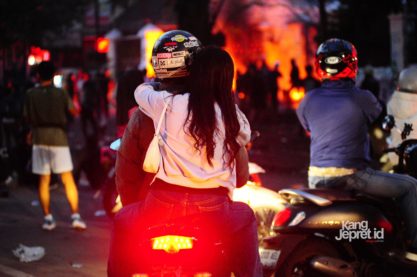 Sepasang sejoli berboncengan di atas motor menonton aksi pembakaran oleh pengunjukrasa di gerbang Gedung DPRD Jawa Barat, Jl Diponegoro, Bandung, Senin (1/9/2025). Aksi unjukrasa beberapa hari berubah menjadi tontonan warga dan pedagang yang mencari peruntungan di keramaian massa. (KANGJEPRET.ID/YOGI ARDHI) (Nikon D700, Nikkor 80-200/2.8 ED 3rd Gen)