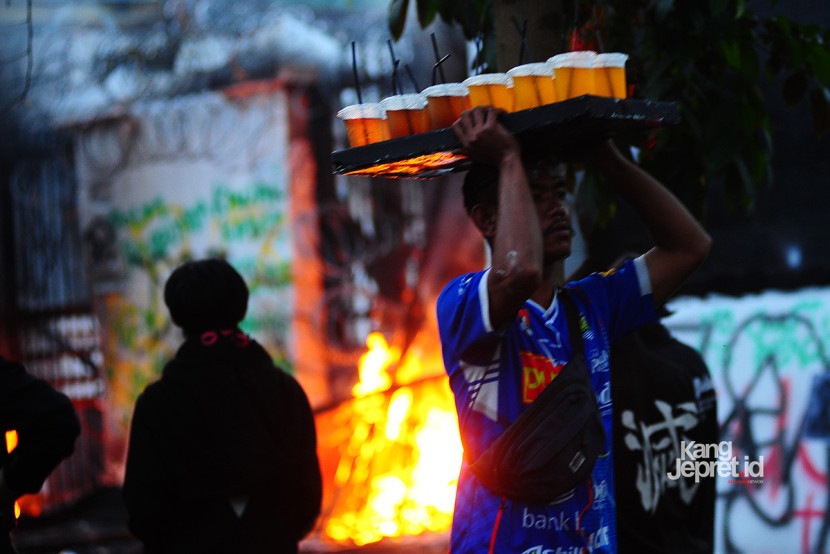 Seorang pedagang minuman melintas di sela aksi pembakaran oleh massa di gerbang Gedung DPRD Jawa Barat, Jl Diponegoro, Bandung, Senin (1/9/2025), Aksi unjukrasa beberapa hari berubah menjadi tontonan warga dan pedagang yang mencari peruntungan di keramaian massa. (KANGJEPRET.ID/YOGI ARDHI) (Nikon D700, Nikkor 80-200/2.8 ED 3rd Gen)