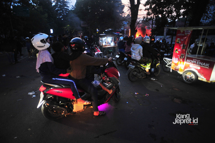 Warga berboncengan membawa anak di atas motor menonton aksi pembakaran oleh pengunjukrasa di gerbang Gedung DPRD Jawa Barat, Jl Diponegoro, Bandung, Senin (1/9/2025). Aksi unjukrasa beberapa hari berubah menjadi tontonan warga dan pedagang yang mencari peruntungan di keramaian massa. (KANGJEPRET.ID/YOGI ARDHI) (Nikon D3, Nikkor 20/2.8 D)