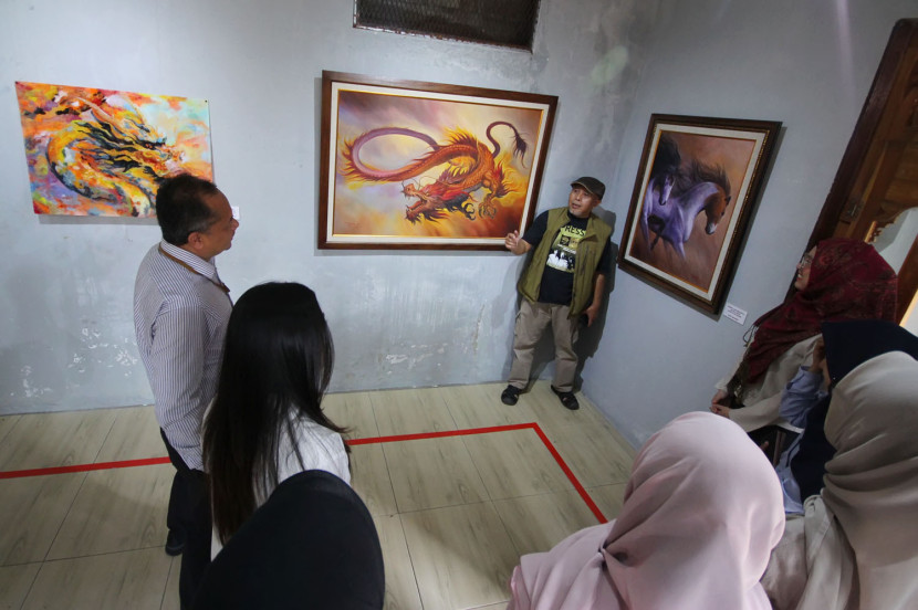 Pelukis Andi Sopiand menjelaskan lukisannya kepada pengunjung di Galeri Lorong Senja, Cijagra, Kota Bandung, Selasa (2/9/2025). Foto: Edi Yusuf