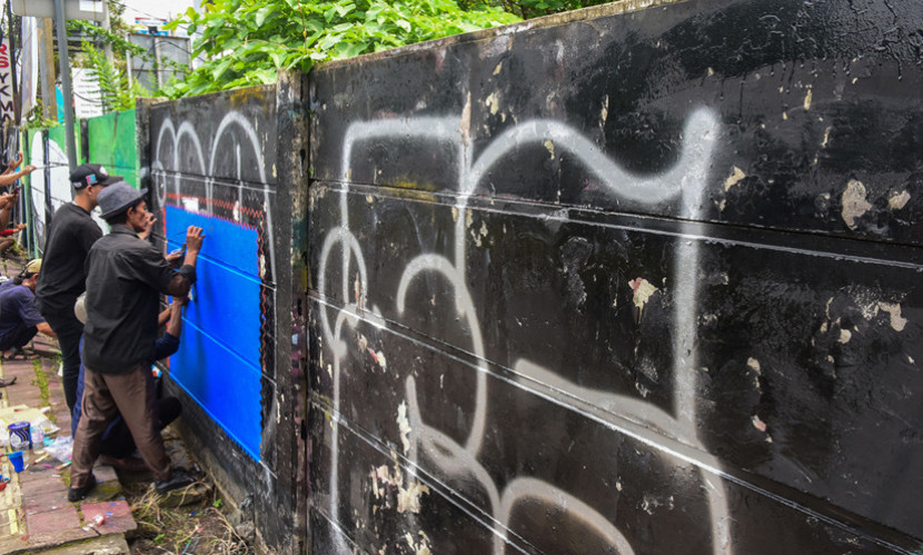 Seniman tengah melukis mural menutupi vandalisme. (FOTO: Ist/Msh)