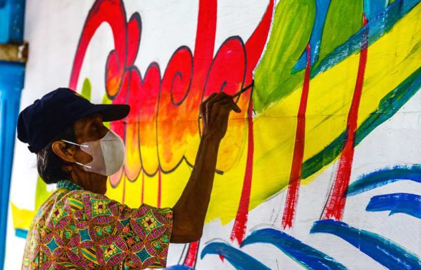 Seorang seniman tengah melukis mural. (FOTO: Ist/Msh)