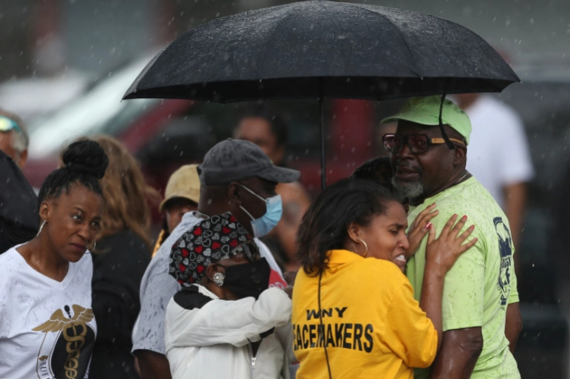 Para pengamat berkumpul di bawah payung saat hujan turun setelah penembakan di supermarket pada Sabtu, 14 Mei, di Buffalo, New York, AS [Joshua Bessex/ AP]