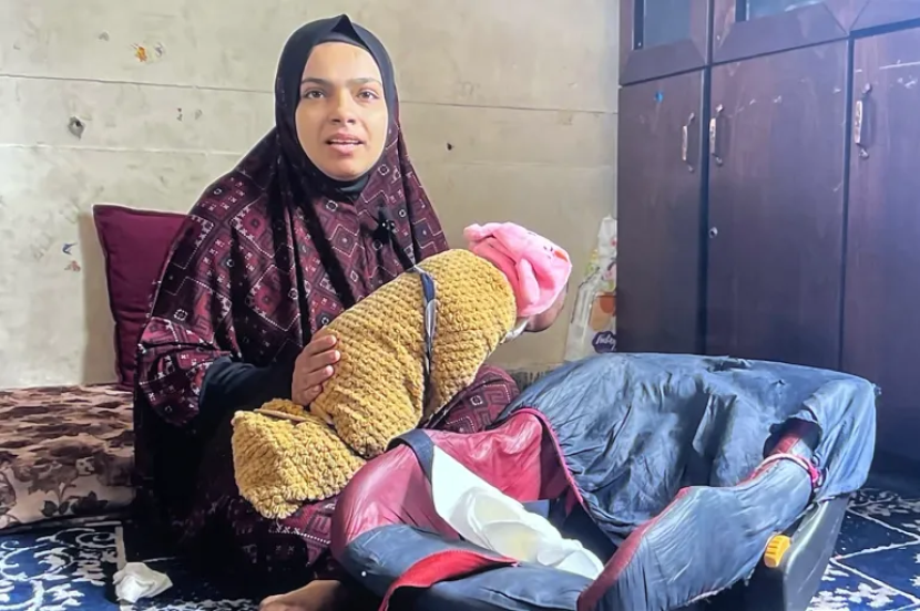 Raeda al-Masry menggendong putranya sambil menceritakan kisah pelariannya ke kamp pengungsi Jabalia dan melahirkan di sekolah tanpa bantuan [Sanad Agency/Al Jazeera]