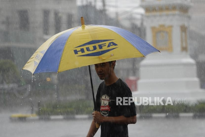 Seorang pria menerobos hujan mengunakan payung. Muhammadiyah memiliki cara sendiri dalam mencegah datangnya hujan, sehingga tak perlu bantuan pawang. Foto: Republika.