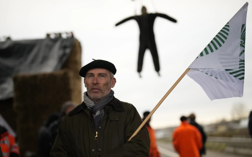 Seorang petani Prancis berdiri dalam barikade unjuk rasa yang memblokir jalan bebas hambatan (30/1/2024). (dok AP News/Christope Ena)