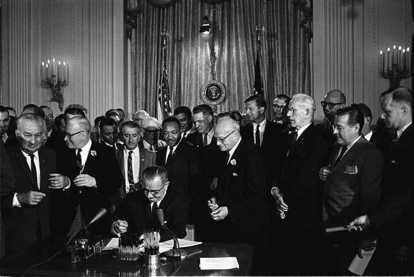 Martin Luther King Jr. berdiri di belakang Presiden AS Lyndon B Johnson saat menandatangani Civil Rights Act pada 1964. (Cecil Stoughton/White House Press Office)