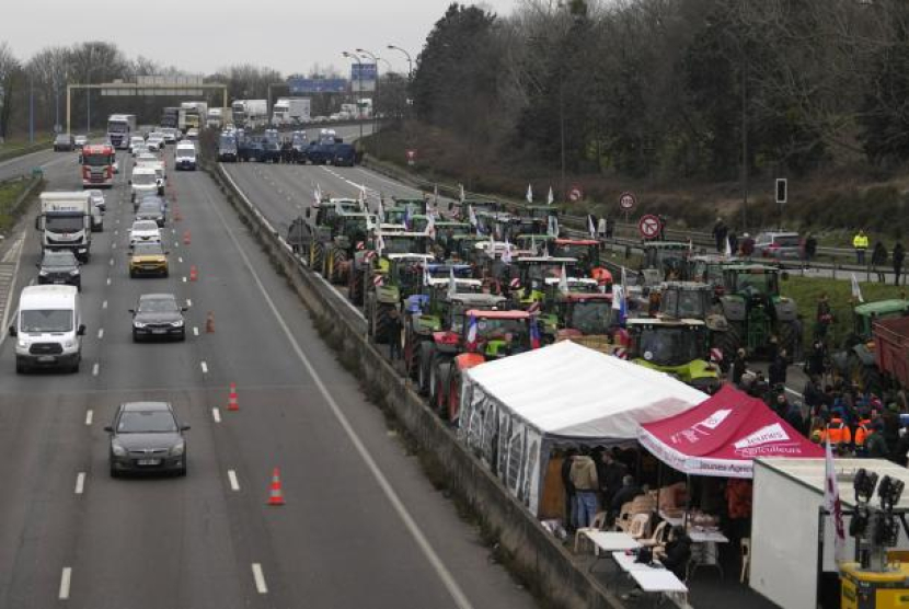 Kendaraan militer, kanan atas, menghadapi petani yang memblokir jalan raya, Rabu, 31 Januari 2024 di Chilly-Mazarin, selatan Paris. 
