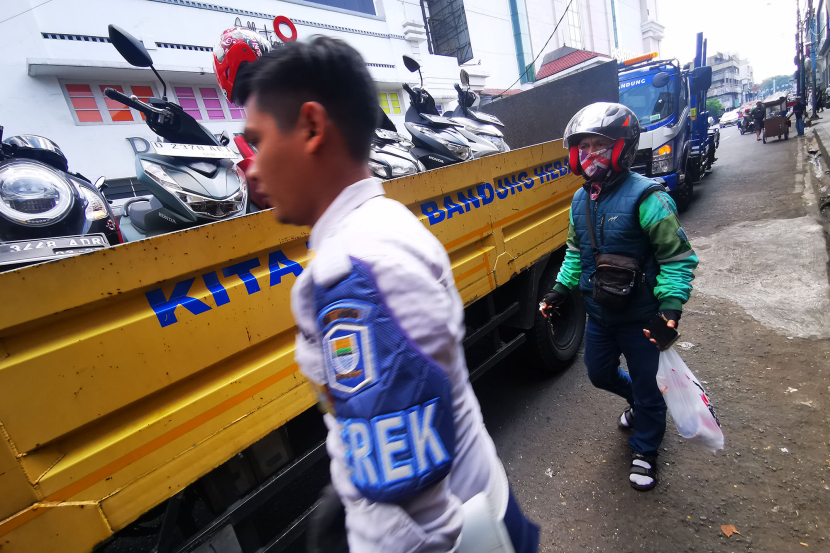 Petugas Dinas Perhubungan meninggalkan pengemudi ojek online yang motornya telah dinaikkan ke atas truk di badan jalan Jl Otto Iskandar Dinata Bandung, Senin (15/7/2024). Pengemudi ojek online ini memarkirkan sepedamotornya saat memesan makanan untuk pelanggannya. (Foto: Yogi Ardhi/KangJepret)