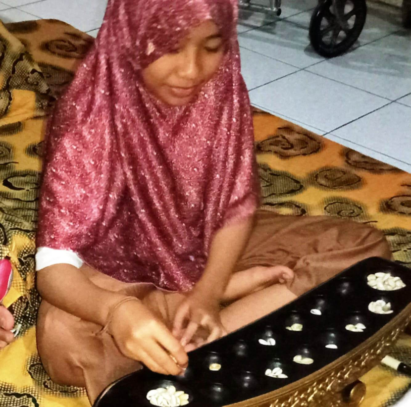 Fayza, anak generasi alfa, memindahkan biji-biji dakon saat bermain dakon bersama adiknya, Arya. Dakon yang digunakan terbuat dari kayu jati yang diperindah dengan hiasan.