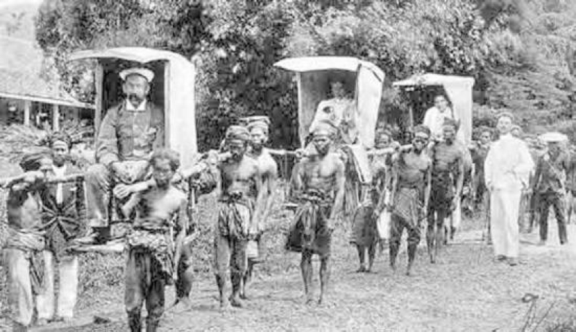 Pribumi  menjadi kuli panggul tandu tuan putih juragan di masa kolonial. 