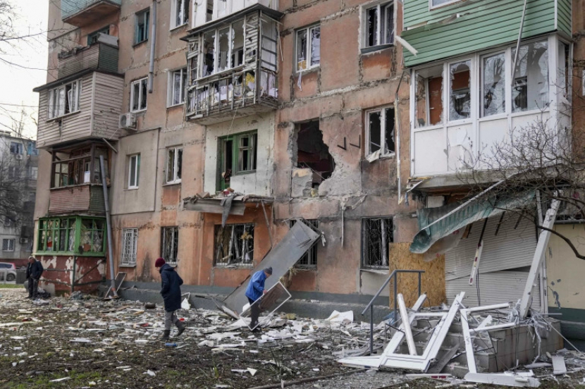 Orang-orang berjalan di sebelah gedung apartemen yang terkena tembakan di Mariupol,