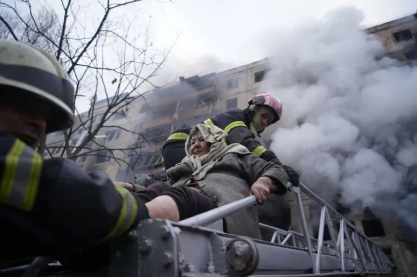 Petugas pemadam kebakaran membantu seorang wanita tua mengungsi dari sebuah apartemen yang terkena tembakan di distrik Obolon Kyiv [Layanan Darurat Negara Ukraina melalui AFP]