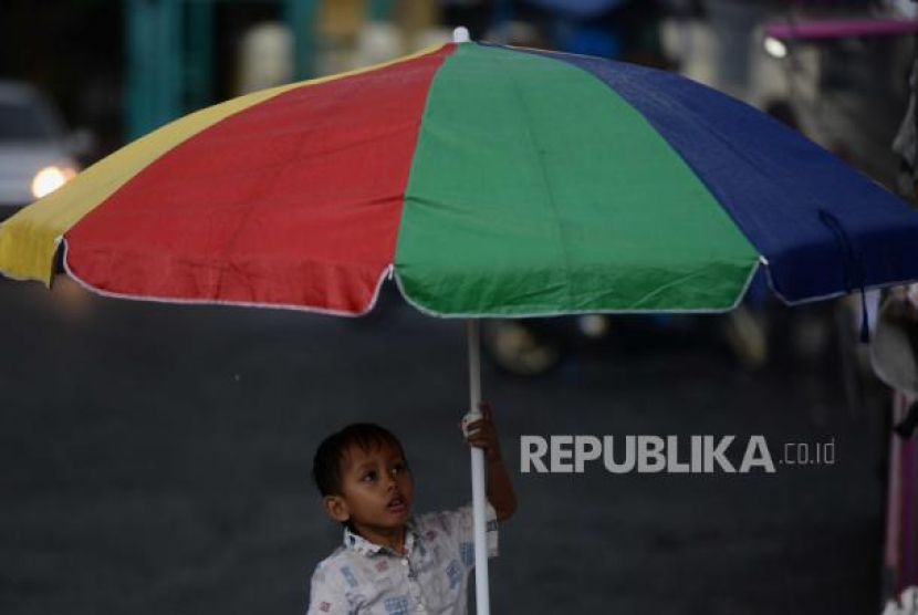 Seorang anak berteduh dibawah payung saat hujan di kawasan Banjir Kanal Timur, Duren Sawit, Jakarta, Senin (27/3/2023). Gelombang Panas Asia: Ciputat Catat Rekor Terpanas di Indonesia, Ini Penjelasan BMKG. Foto: Republika/Putra M. Akbar