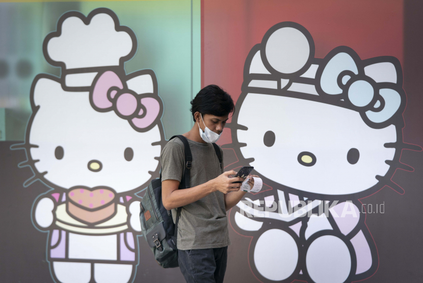 Seorang pria yang mengenakan masker berjalan melewati iklan Hello Kitty di luar sebuah toko serba ada di Kuala Lumpur, Malaysia. AP/Vincent Thian 