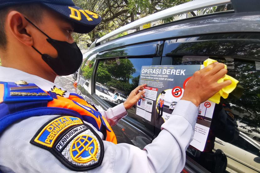 Petugas Dinas Perhubungan memasang stiker di jendela mobil yang terparkir di badan jalan Jl Wastukencana Bandung, Senin (15/7/2024). Identitas mobil ini difoto oleh polisi lalu lintas kemudian dinput ke dalam aplikasi tilang elektronik Polda Jabar. (Foto: Yogi Ardhi/KangJepret)