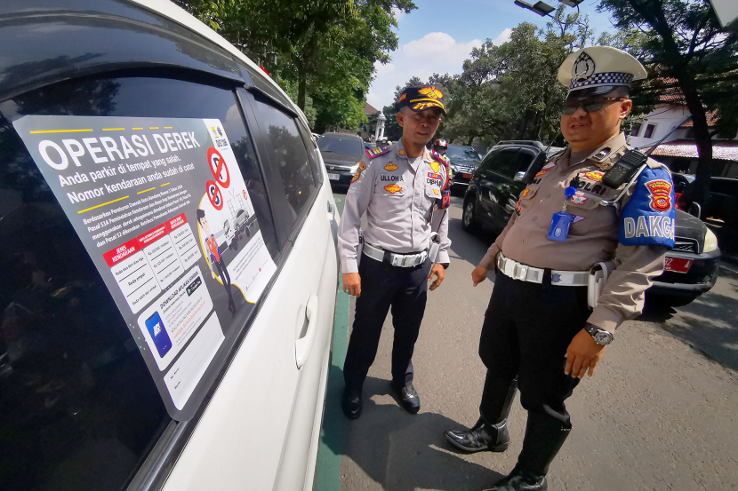 Petugas Dinas Perhubungan memasang dan polisi memperhatikan stiker di jendela mobil yang terparkir di badan jalan Jl Wastukencana Bandung, Senin (15/7/2024). Identitas mobil ini difoto oleh polisi lalu lintas kemudian dinput ke dalam aplikasi tilang elektronik Polda Jabar. (Foto: Yogi Ardhi/KangJepret)