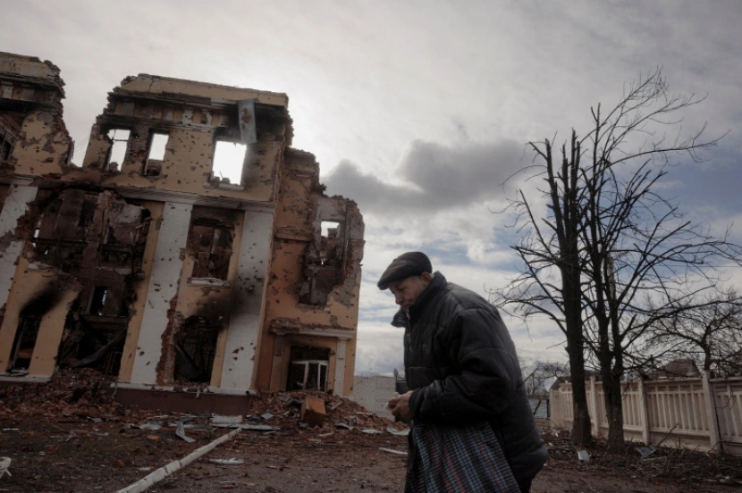 Seorang lelaki tengah berjalan dengan suasana ibu kota Kyiv yang muram dengan banyaknya bangunan runtuh akibat serangan Rusia.
