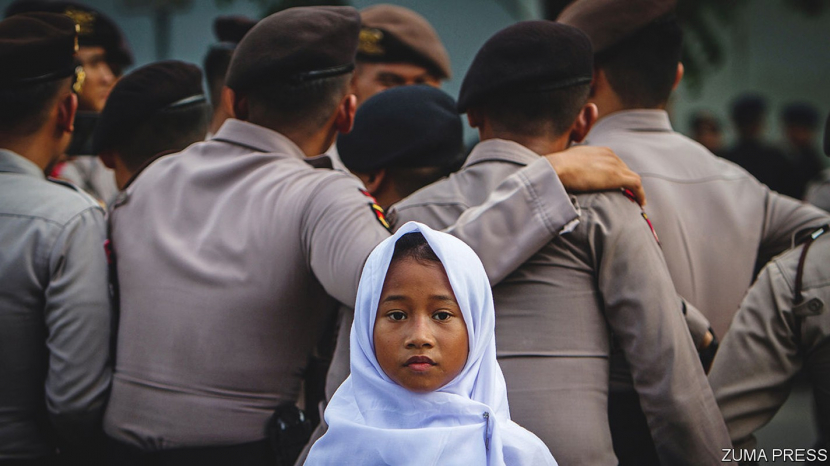 Gadis cilik memakai jilbab  berfoto di dekat kerumunan petigas keamanan. (lustrasi/The Economis)