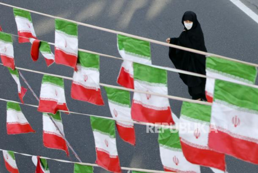 Seorang wanita iran berjalan di depan deretan bendera negara tersebut. 