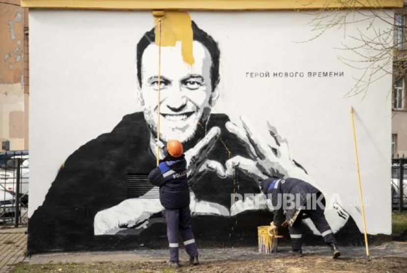 Para pekerja kota mengecat grafiti pemimpin oposisi Rusia yang dipenjara Alexei Navalny di St Petersburg, Rusia, Rabu, 28 April 2021. 