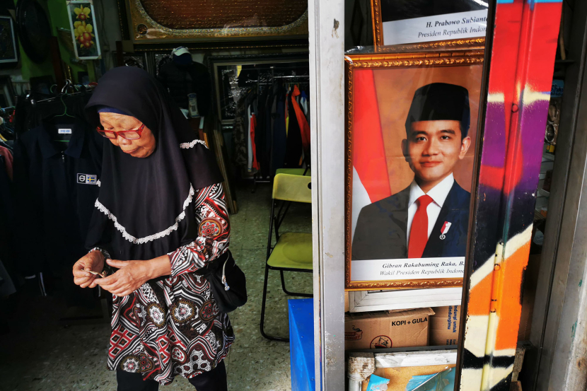 Seorang wanita penjaga kios melintasi foto Presiden dan Wakil Presiden RI terpilih, Prabowo Subianto dan Gibran Rakabuming Raka terpampang di kios pedagang lukisan dan bingkai di Jalan Veteran, Bandung, Rabu (22/5/2024) (FOTO: YOGI ARDHI/REPUBLIKA NETWORK)
