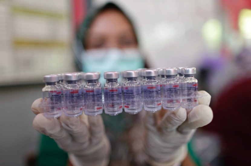 Seorang petugas kesehatan wanita bermasker memegang botol bekas vaksin Sinovac ke depan  kamera. Sekitar 79 persen dari mereka yang divaksinasi di Indonesia telah menerima suntikan Sinovac. Sementara semua vaksin terbukti kurang efektif melawan Omicron, beberapa penelitian menemukan vaksin yang tidak aktif seperti Sinovac tidak menghasilkan antibodi penetral sama sekali [File: Adi Weda/EPA]