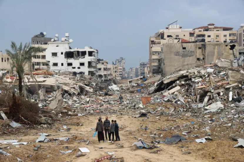 Warga Palestina berjalan melewati gedung yang hancur akibat pemboman Israel di Jalur Gaza di Kota Gaza pada 3 Januari 2024. [File: Mohammed Hajjar/AP]