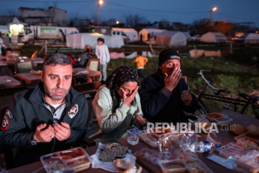 Orang-orang menyantap makanan berbuka puasa yang disediakan untuk berbuka puasa pada hari pertama Ramadhan, di Adiyaman, Turki, (23/3/2023). Lebih dari 50.000 orang tewas dan ribuan lainnya terluka setelah gempa bumi besar melanda Turki selatan dan Suriah utara pada 06 dan 20 Februari 2023. Foto: EPA-EFE/ERDEM SAHIN