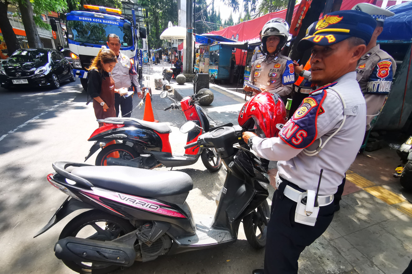 Petugas Dinas Perhubungan dan polantas menindak pemilik motor yang memarkirkan sepeda motornya di badan jalan Jl Purnawarman Bandung, Senin (15/7/2024). (Foto: Yogi Ardhi/KangJepret)