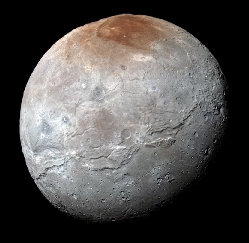 Tampilan warna yang disempurnakan dari bulan terbesar Pluto, Charon. Warna diproses untuk menonjolkan variasi sifat permukaan di bulan, paling mencolok adalah wilayah kutub utara (atas) yang kemerahan. Kredit: NASA/JHUAPL/SwRI