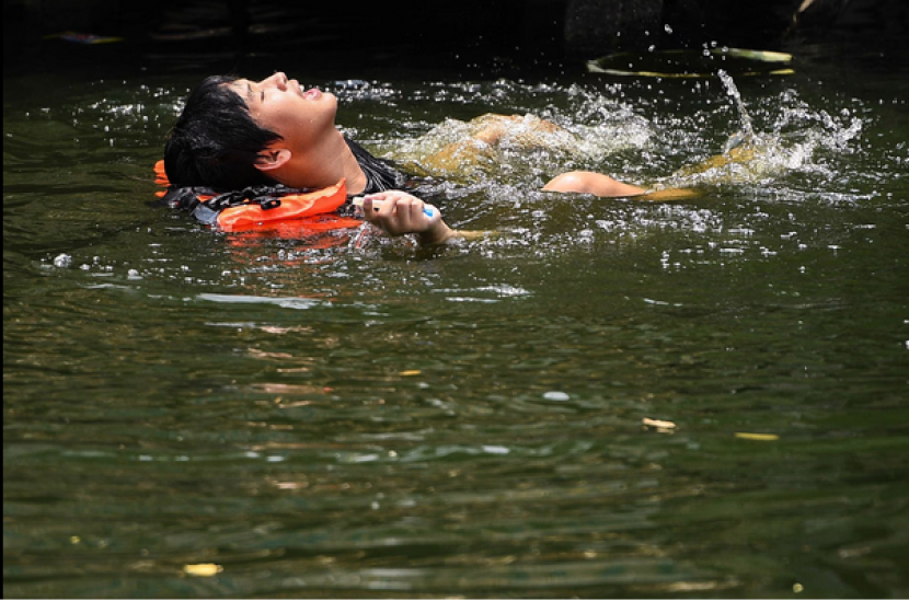 Seorang pria berenang di kanal di tengah suhu panas ekstrem 45,5 derajat Celsius di Bangkok, Thailand, 22 April 2023. Foto: REUTERS/Chalinee Thirasupa