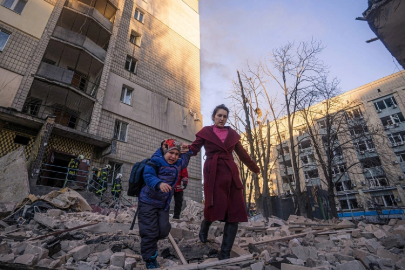 Seorang wanita dengan seorang anak dievakuasi dari sebuah bangunan tempat tinggal yang rusak akibat penembakan, saat serangan Rusia di Ukraina berlanjut [Layanan Darurat Negara via Reuters]