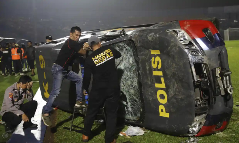 Polisi Indonesia dengan kendaraan yang rusak di lapangan stadion Kanjuruhan di Malang, Jawa Timur, setelah bentrokan antara pendukung tim lawan. Foto: Yudha Prabowo/AP
