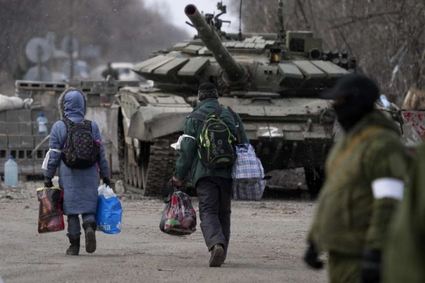 Warga sipil Mauripol berjalan untuk mengungsi melewati kendaraan berat militer, Mariupol adalah salah satu kota yang menjadi ajang pertempuran invasi Rusia ke Ukraina. [Anadolu Agency]